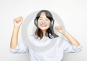 Pretty smiling Asian teenage girl listens to music on headphones over white background.