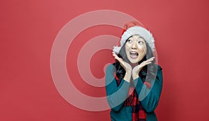 Pretty smiling asian woman in warm christmas sweater and santa hat is having excitement on red background for season celebration