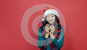 Pretty smiling asian woman in warm christmas sweater and santa hat is having hot chocolate on red background for season