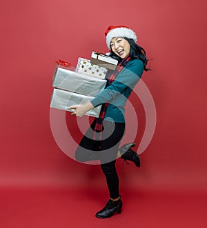 Pretty smiling asian woman in warm christmas sweater and santa hat holding gift box as present with red background for season