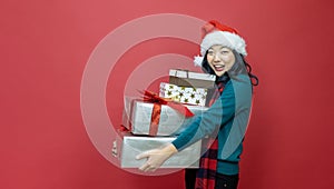 Pretty smiling asian woman in warm christmas sweater and santa hat holding gift box as present with red background for season