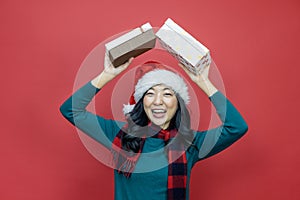 Pretty smiling asian woman in warm christmas sweater and santa hat holding gift box as present with red background for season