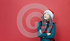 Pretty smiling asian woman in warm christmas sweater and santa hat looking side way with red background for season celebration