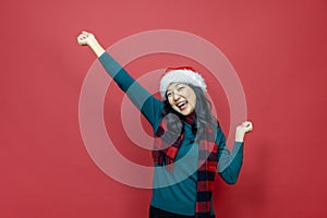 Pretty smiling asian woman in warm christmas sweater and santa hat on red background for season celebration concept