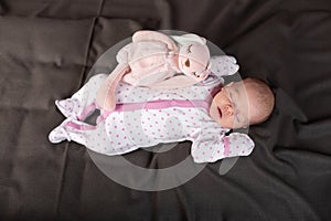 Pretty smiling baby girl and toy rabbit lying in darck background