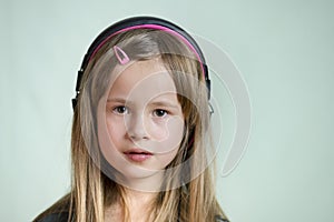 Pretty smiling cild girl listening to music in big pink earphones