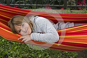 Pretty smiling fair little girl in grey sweater looking out from a colourful hammock