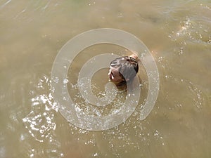 A pretty smiling girl of 6-7 years old is swimming in the water. Wet hair on the head. Laughing baby face. Serbia, Sava river,