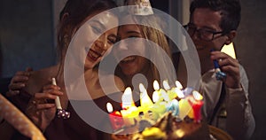 Pretty smiling girl blows out candles on a birthday cake surrounded by friends at a party. around the atmosphere of the