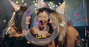 Pretty smiling girl blows out candles on a birthday cake surrounded by friends at a party. around the atmosphere of the