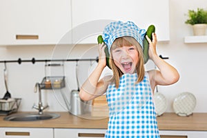 Pretty smiling girl in cook clothes funs with cucumbers