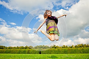 Pretty smiling girl is jumping on green meadow