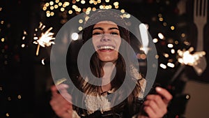 Pretty smiling girl in winter clothes, rejoicing, looking to camera. Woman holding sparklers and dancing, standing in