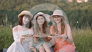 Pretty smiling girls, sitting on the grass and demonstrating snails on wooden plates