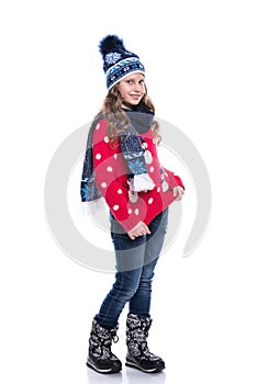 Pretty smiling little girl with curly hairstyle wearing knitted sweater, scarf and hat with skates isolated on white background.
