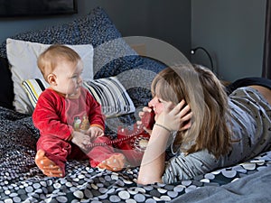 Pretty smiling little girl lying on bed playing with vintage red telephone and her cute chubby baby sister