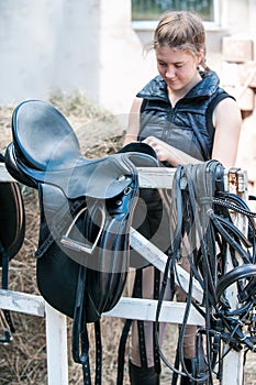 Pretty smiling teenage girl equestrian cleans black Leather Horse Saddle