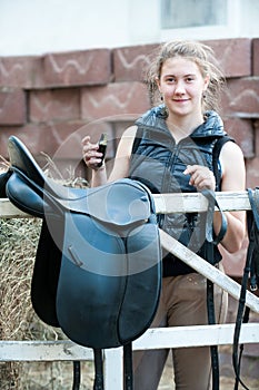 Pretty smiling teenage girl equestrian cleans black Leather Horse Saddle