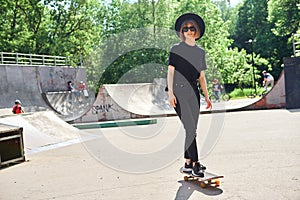 Pretty smiling teenage girl in hat ans sunglasses rides skateboard in skatepark, active and sport lifestyle