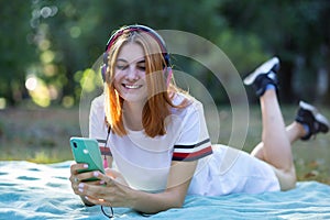 Pretty smiling teenage girl listening to music in pink earphones and using sellphone outdoors