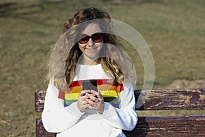 Pretty smiling teenager girl chating with online firends. Happy curly young girl wear rainbow sweater