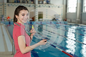 Pretty smiling trainer woman holding a stopwatch on poolside