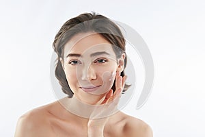 Pretty smiling woman applying cream on face