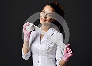 Pretty smiling woman doctor gynecologist or nurse in pink latex gloves and uniform stands holding medical bandage