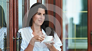 Pretty smiling woman having break outdoor drinking hot coffee or tea holding cup and saucer by hands