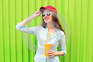 Pretty smiling woman in sunglasses with cup of fruit juice over colorful green