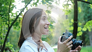 Pretty smiling woman wedding photographer wearing white shirt is making photos with professional camera in a park on a
