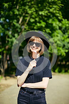 Pretty smiling young female in sunglasses and hat eating ice cream in the park, photography for blog or ad photo