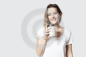 Pretty smiling young woman blonde hair with disposal paper cup of coffee, white background isolated.