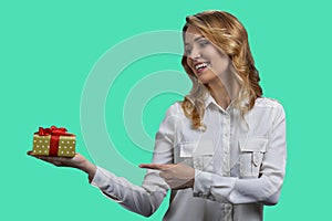 Pretty smiling young woman pointing at gift box in her hand.