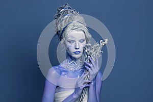 Pretty Snow Queen or Winter Witch woman with perfect fantasy makeup and painted body on blue background. Carnival and Halloween