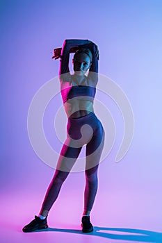 Pretty sporty woman with perfect body standing isolated on purple light background