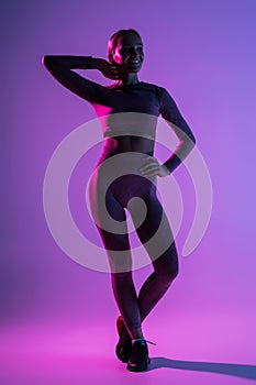 Pretty sporty woman with perfect body standing  on purple light background