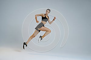 Pretty sporty woman running in Mid-Air exercising during cardio workout over studio background