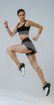 Pretty sporty woman running in Mid-Air exercising during cardio workout over studio background