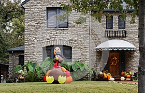 Pretty stone house with awning and fall wreath on door and many pumpkins on porch and big blowup turkey in landscaped front yard