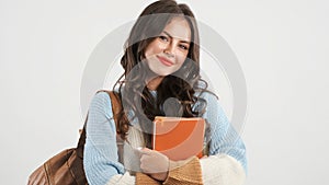 Pretty student girl with backpack and book happily looking in camera over white background