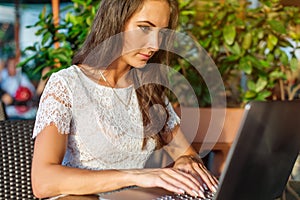 Pretty student girl surfing the internet on her laptop while sitting at outdoor cafe. Young business woman working