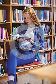 Pretty student sitting on chair reading book in library