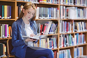 Pretty student sitting on chair reading book in library