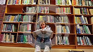 Pretty student sitting on floor reading book in the library