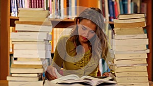 Pretty student studying in the library surrounded by books