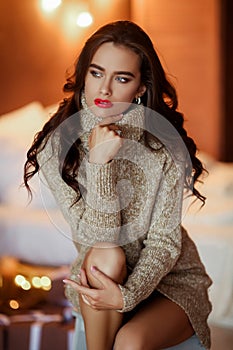 Pretty stylish girl in dress with hairstyle and makeup sitting at sofa. Fashion glamour portrait.