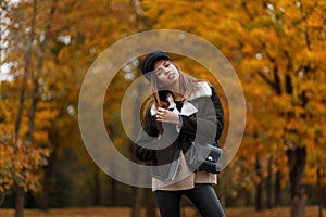 Pretty stylish model of a young woman in fashionable clothes in an elegant hat with a leather handbag posing in the park on an