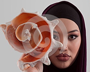 Pretty stylish Muslim woman wearing hijab and holding a seashell and dreams closed eyes. Golden ratio and ideal