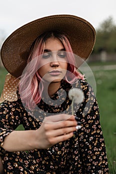 Pretty stylish young woman with colored hair in vintage fashion straw hat in beautiful youth black summer dress holds in hand